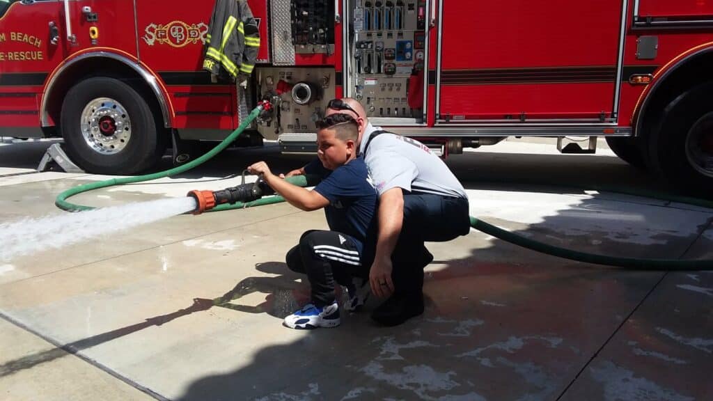 young boy with a fire fighter using the water hose